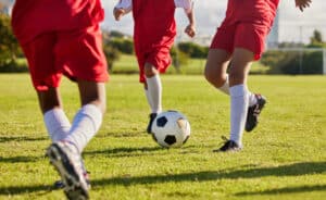Kids team, soccer or legs with soccer ball in workout, fitness game or exercise on nature park grass, high school stadium or field. Football or sports training with energy in health or girls wellness